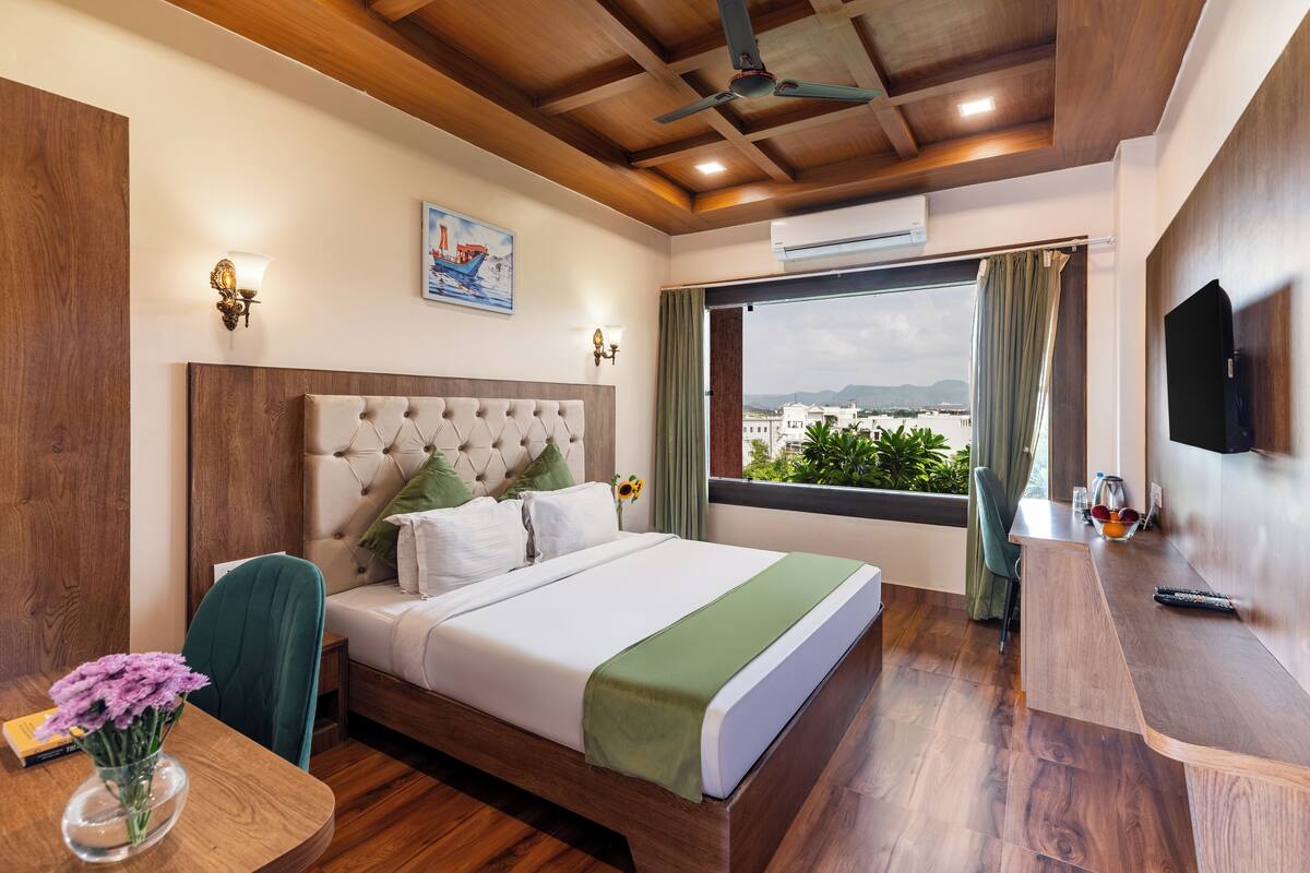 A hotel room with a bed, a desk, a TV, and a window with a view.
