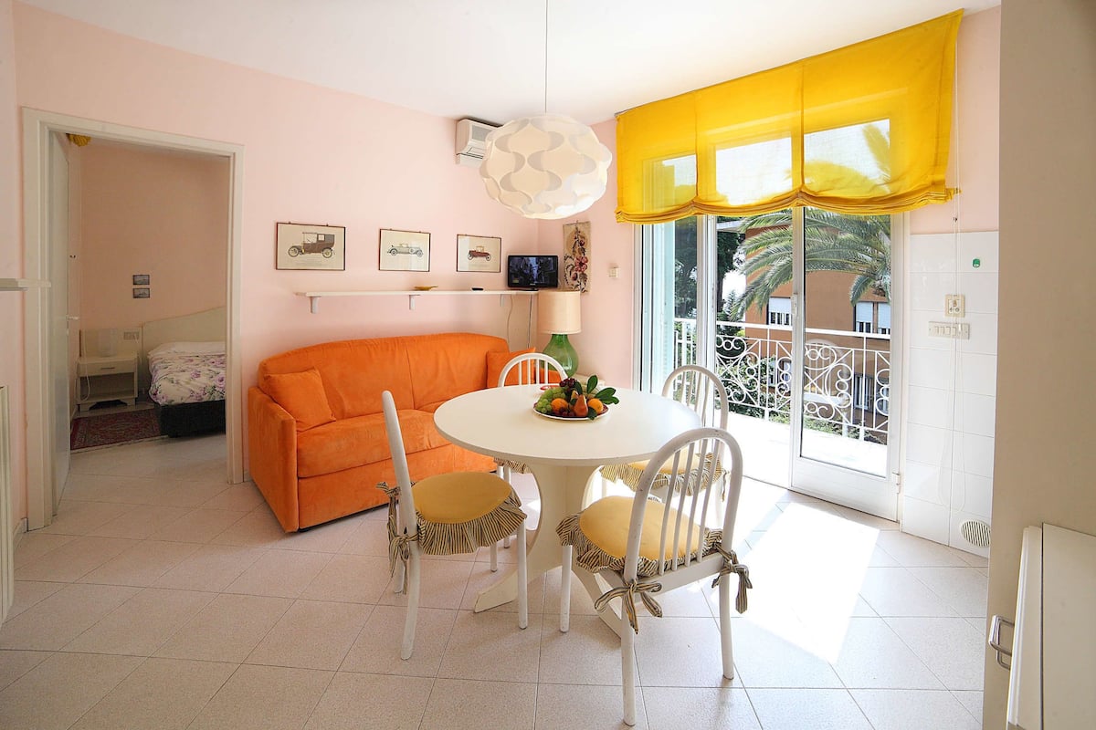 Un comedor con una mesa redonda, sillas blancas y un valance amarillo en la ventana.