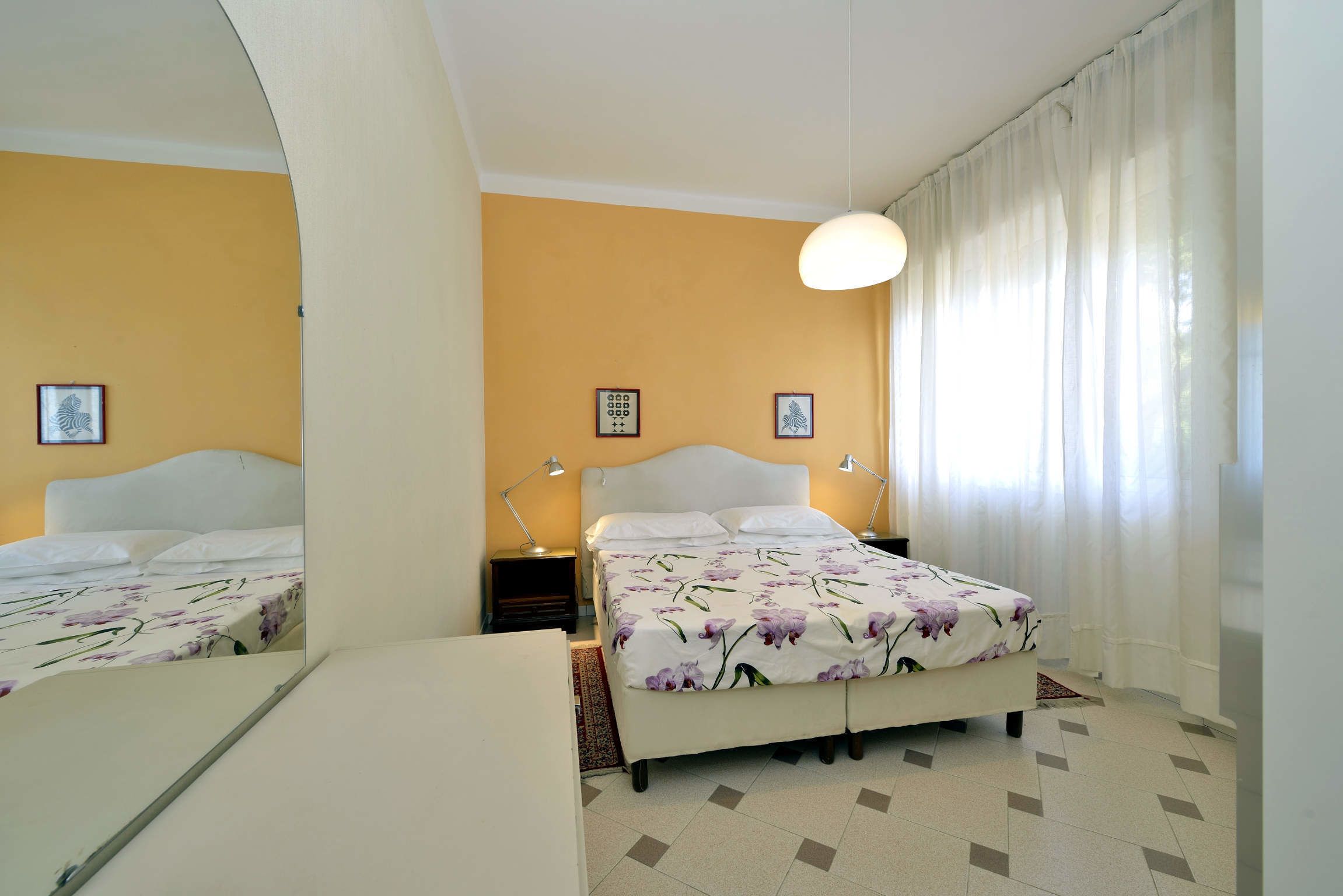 Una camera da letto con un letto, comodini, uno specchio e una finestra con tende.