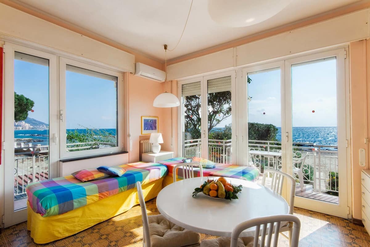 Una habitación con balcón, una mesa con fruta y una cama con ropa de cama colorida.