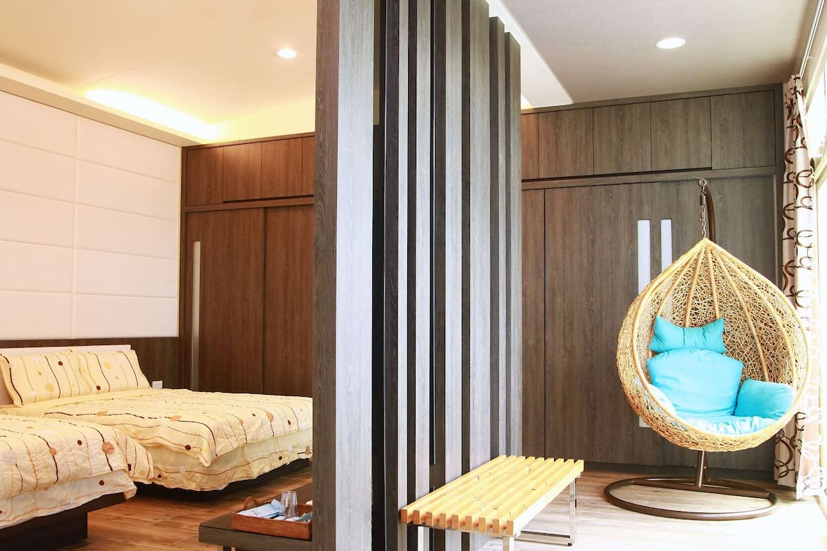 A modern bedroom with a bed, a hanging chair, and a bench.
