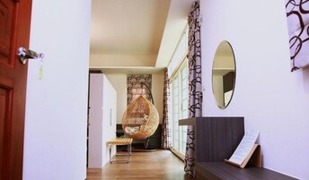 Un pasillo con una mecedora de mimbre, un banco, un espejo adosado a la pared y un atril para menús.