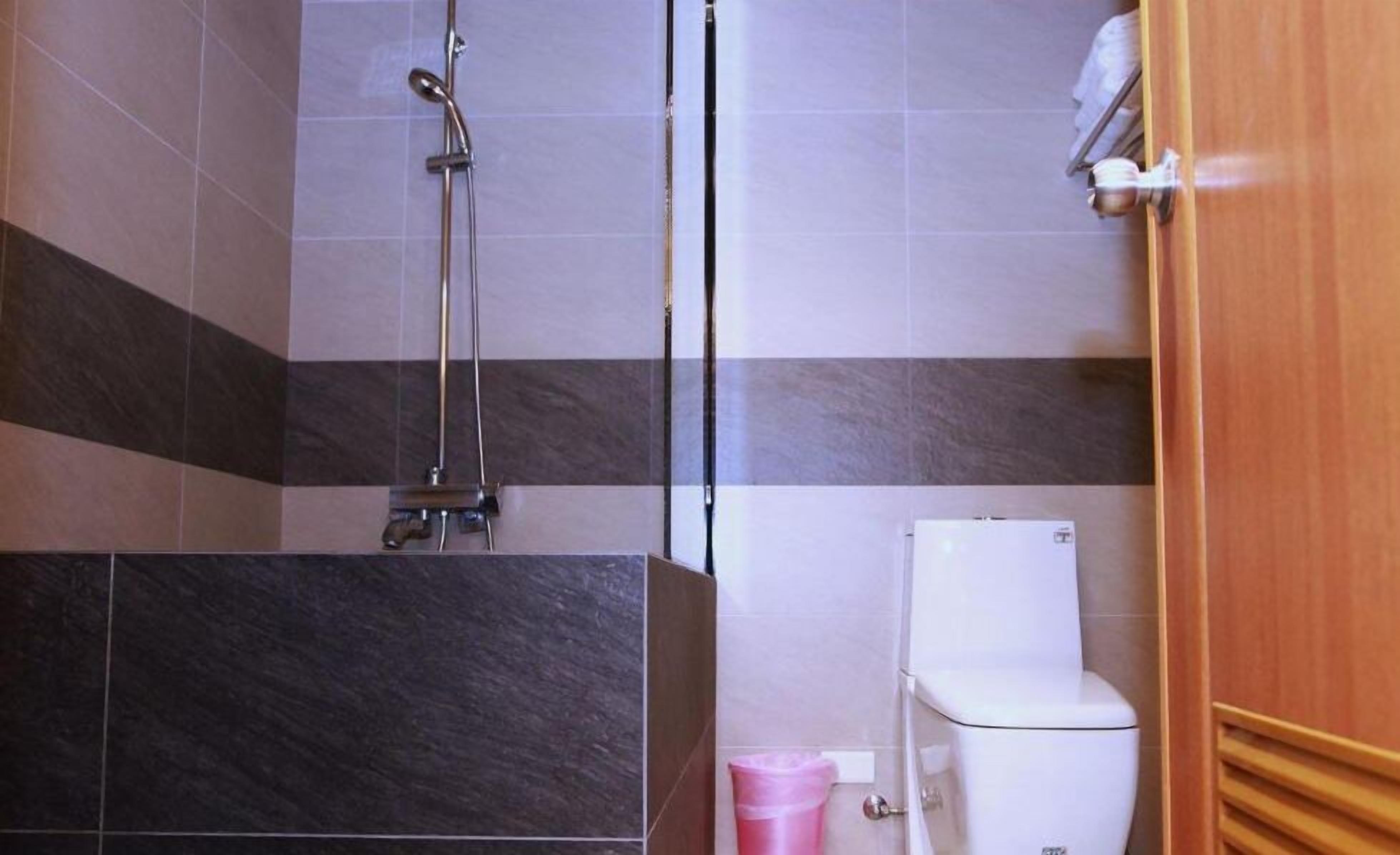 A bathroom with a shower, toilet, and a trash bin.