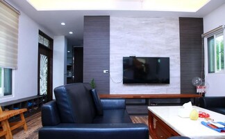 Una sala de estar moderna con un sofá de cuero negro, un televisor de pantalla plana montado en la pared y una mesa de centro de madera.