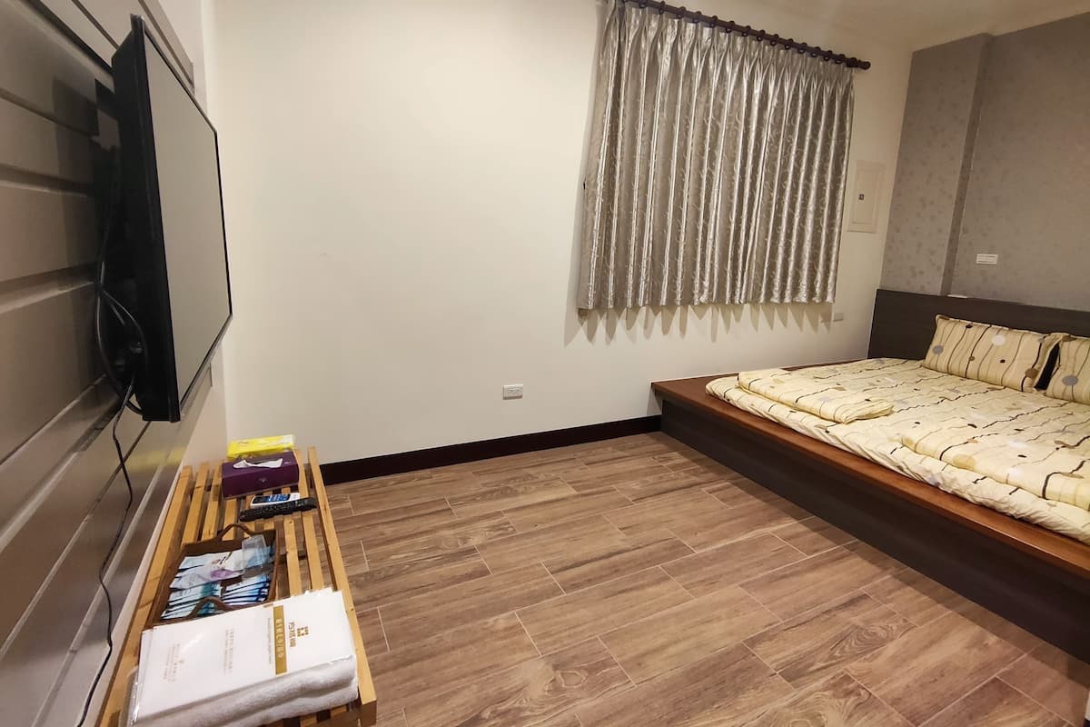 A bedroom with a bed, a wooden bench with items, a TV, and a window with curtains.