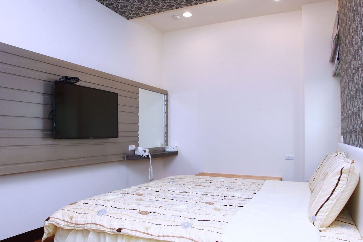 A bedroom with a bed, a mounted TV, and a bedside table.