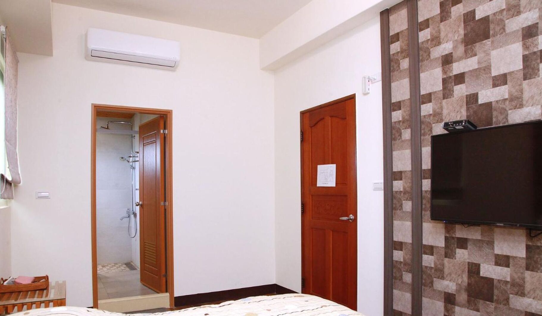 A bedroom with a bed, a wooden door, a shower, and a mounted television.