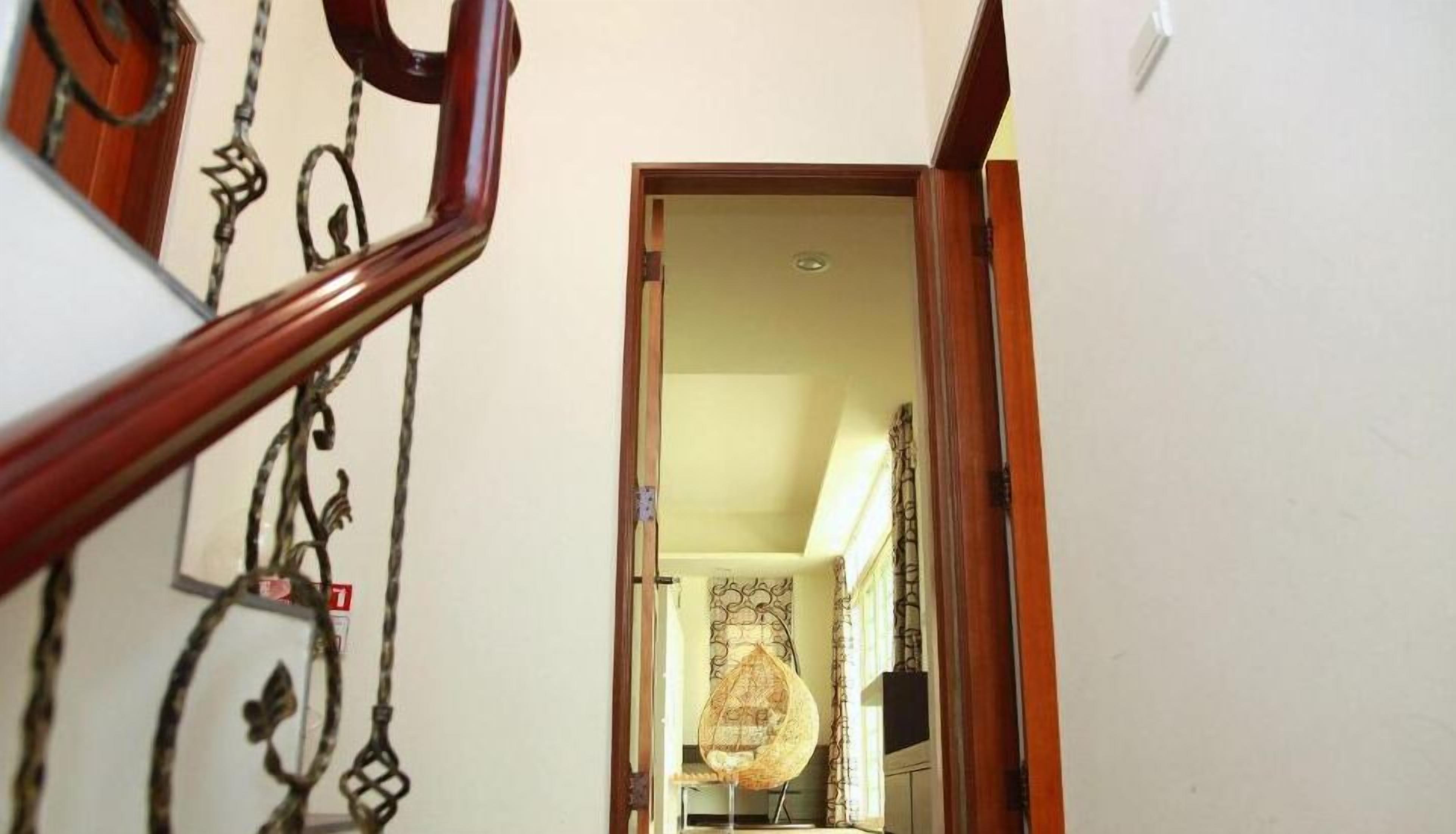 A hallway with a wooden handrail and a door leading to a room with a hanging light fixture.