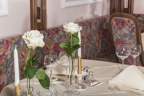 A dining table set with white roses, clear wine glasses, and a gold candle holder. - Hotel Bergland Obsteig (Obsteig)