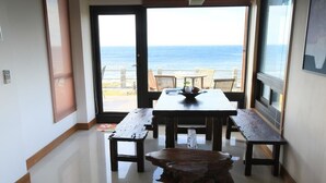 Un área de comedor con una mesa y bancos, una mesa de centro de madera, y vista al océano a través de amplios ventanales.