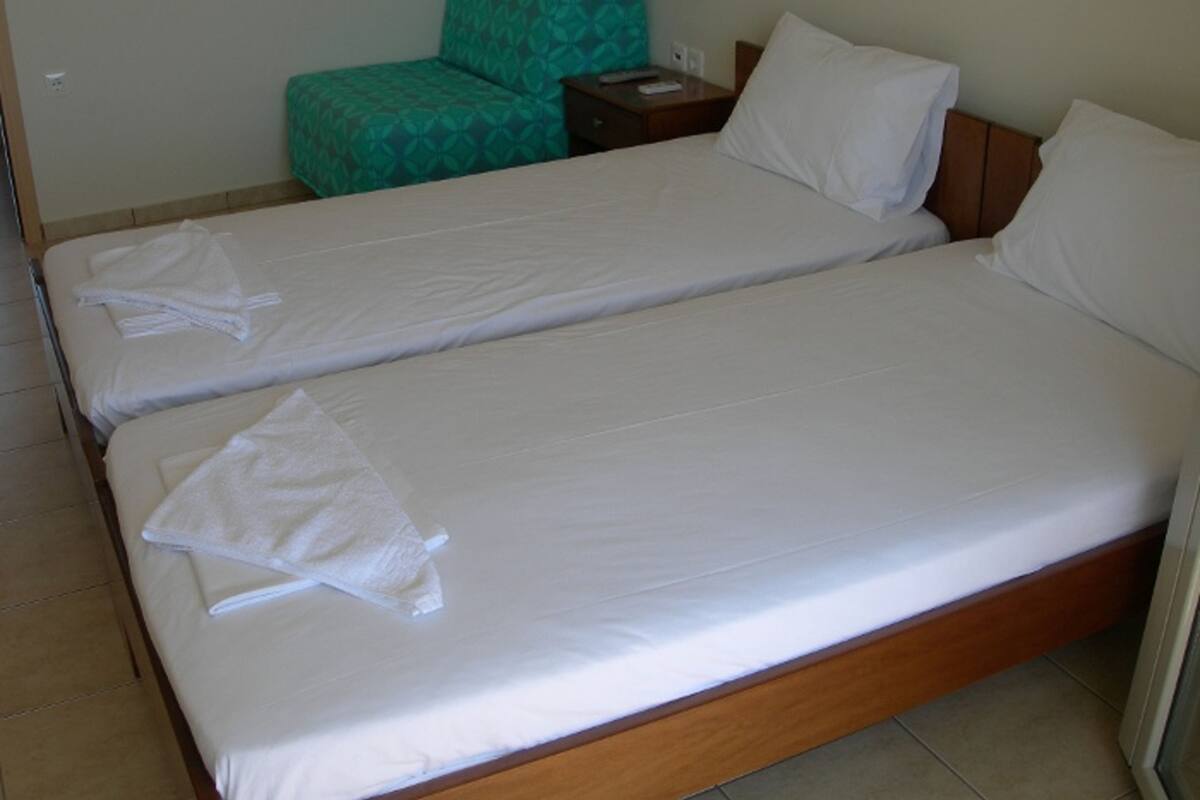 A hotel room with two single beds, a green armchair, and a wooden nightstand.