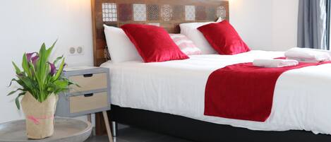 A neatly made bed with red and white bedding, a small round table with a plant, and a nightstand with drawers.