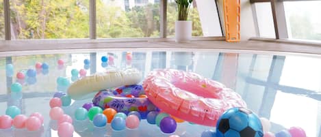 Una habitación con un ventanal grande, una planta en maceta y una mesa de vidrio con globos de colores y una pelota de fútbol.