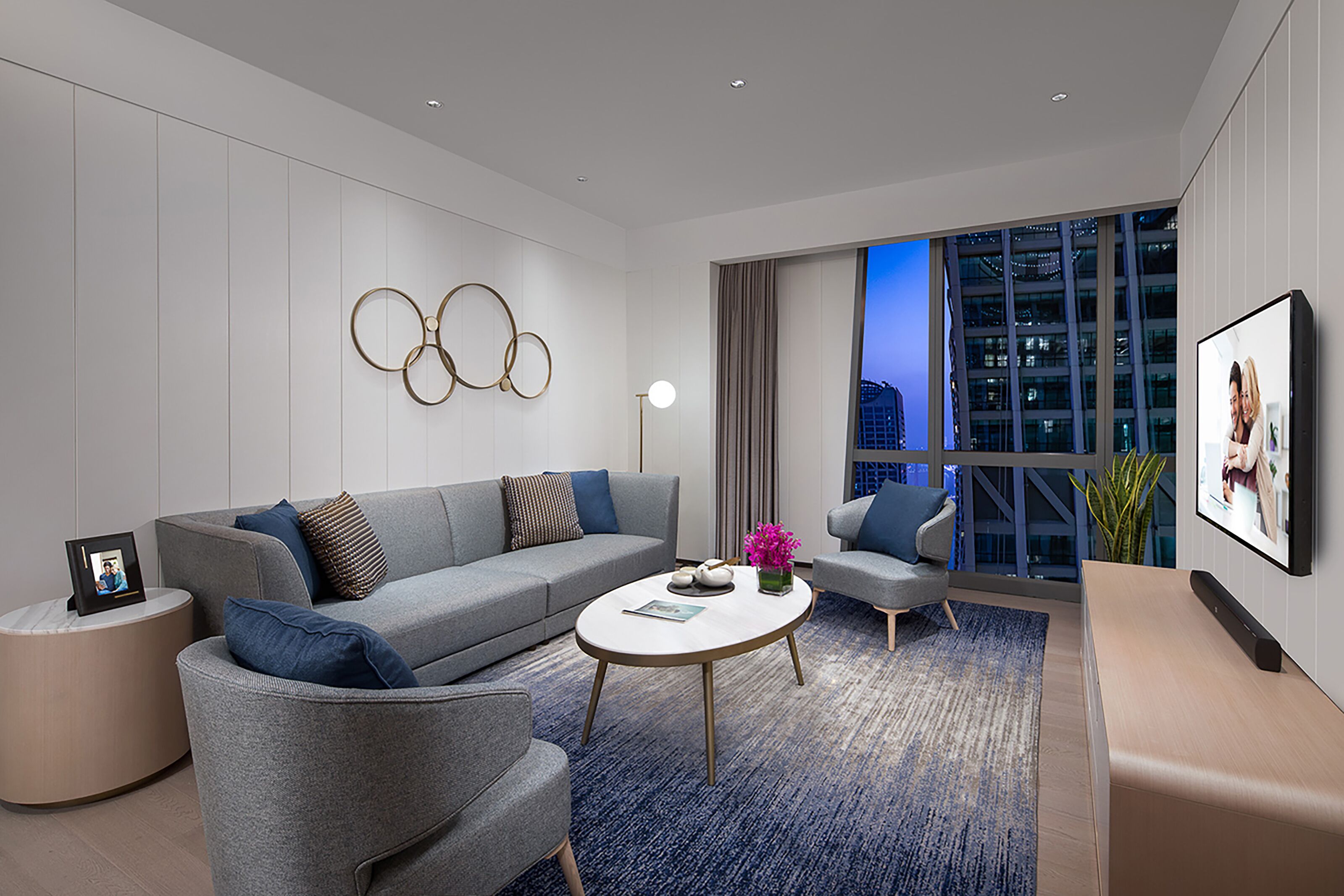A modern living room with a grey sofa, a round coffee table, and a city view through large windows.