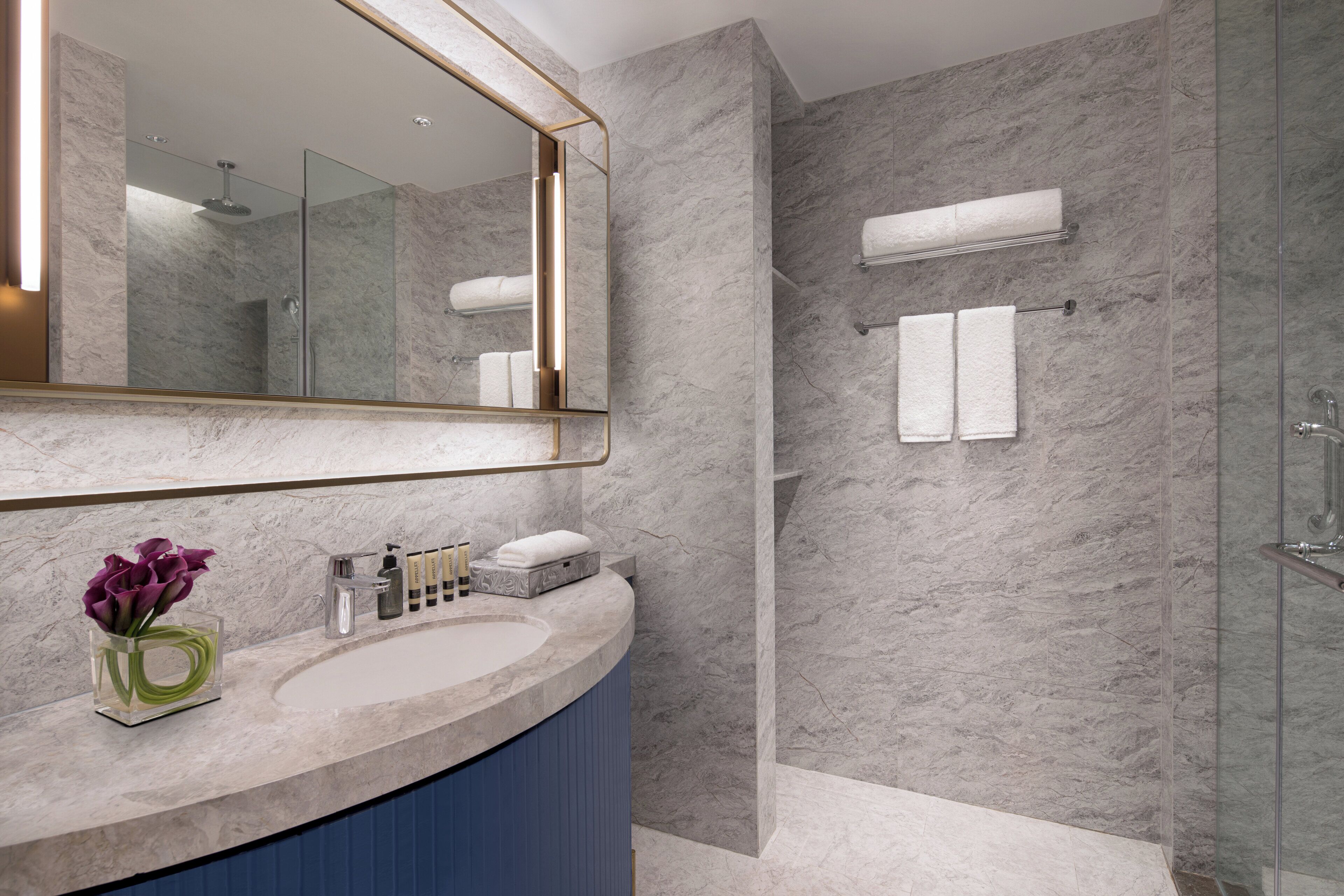 Un baño moderno con encimera de mármol, un espejo grande y una cabina de ducha de vidrio.
