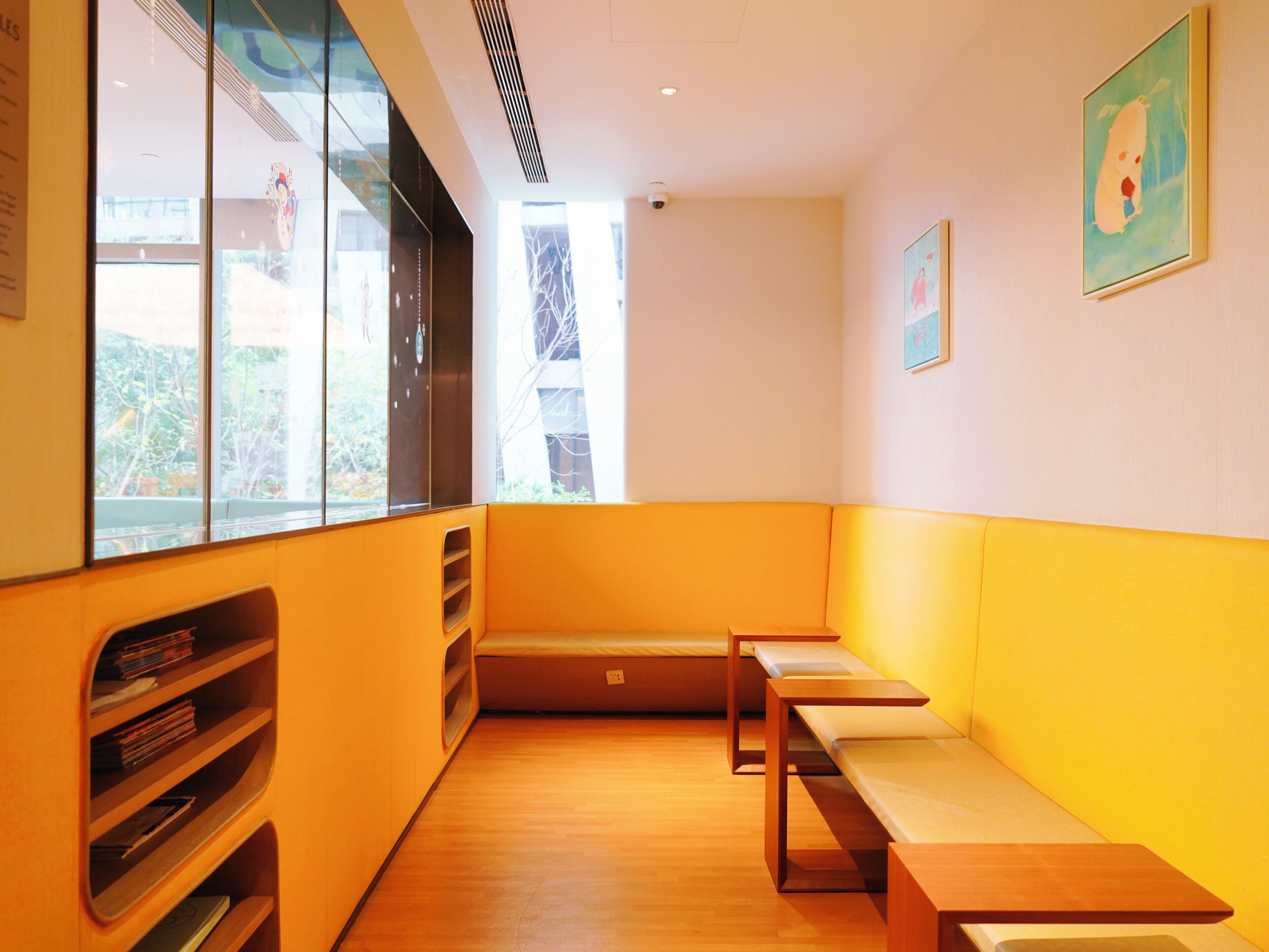 Una habitación con un banco de madera, una estantería y un ventanal con vistas a árboles.