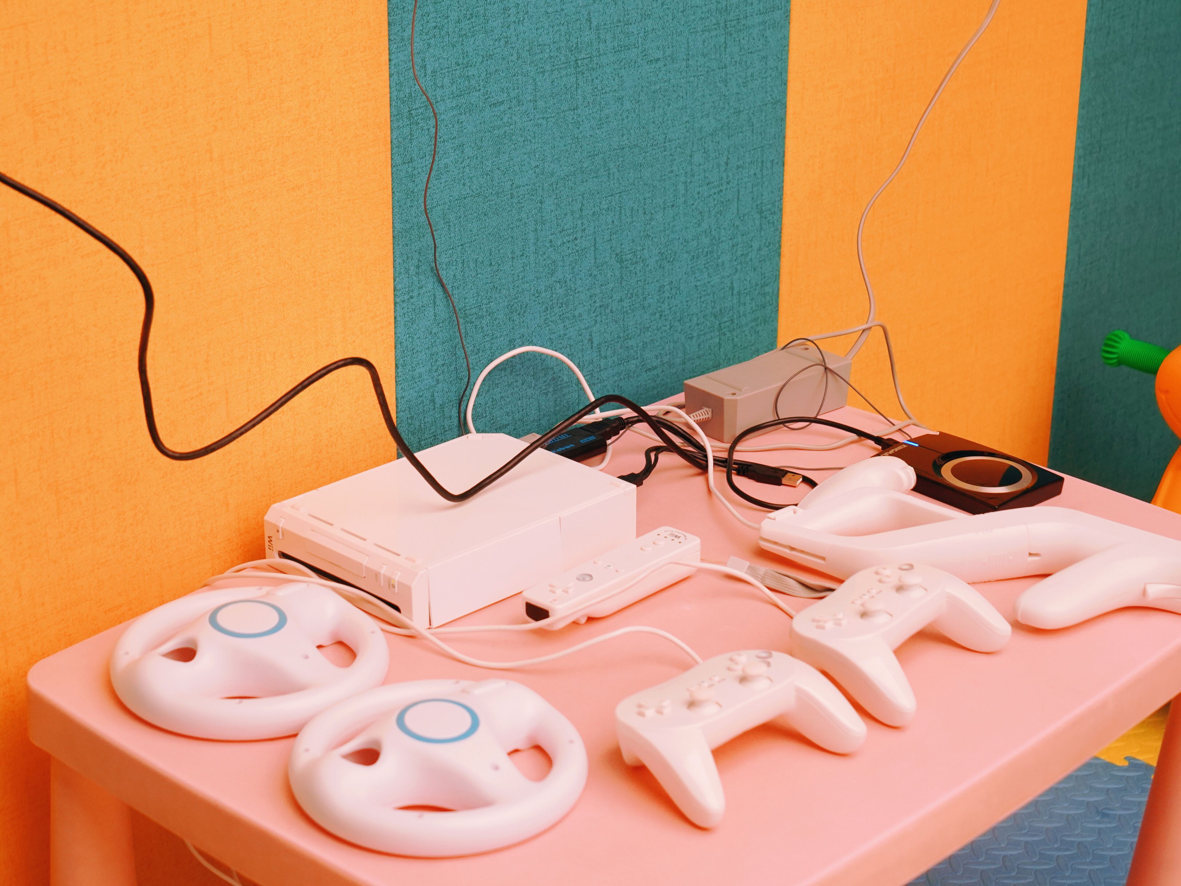 A pink table with a white gaming console, two white controllers, and a white charging cable.