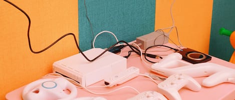 A pink table with a white gaming console, two white controllers, and a white charging cable.