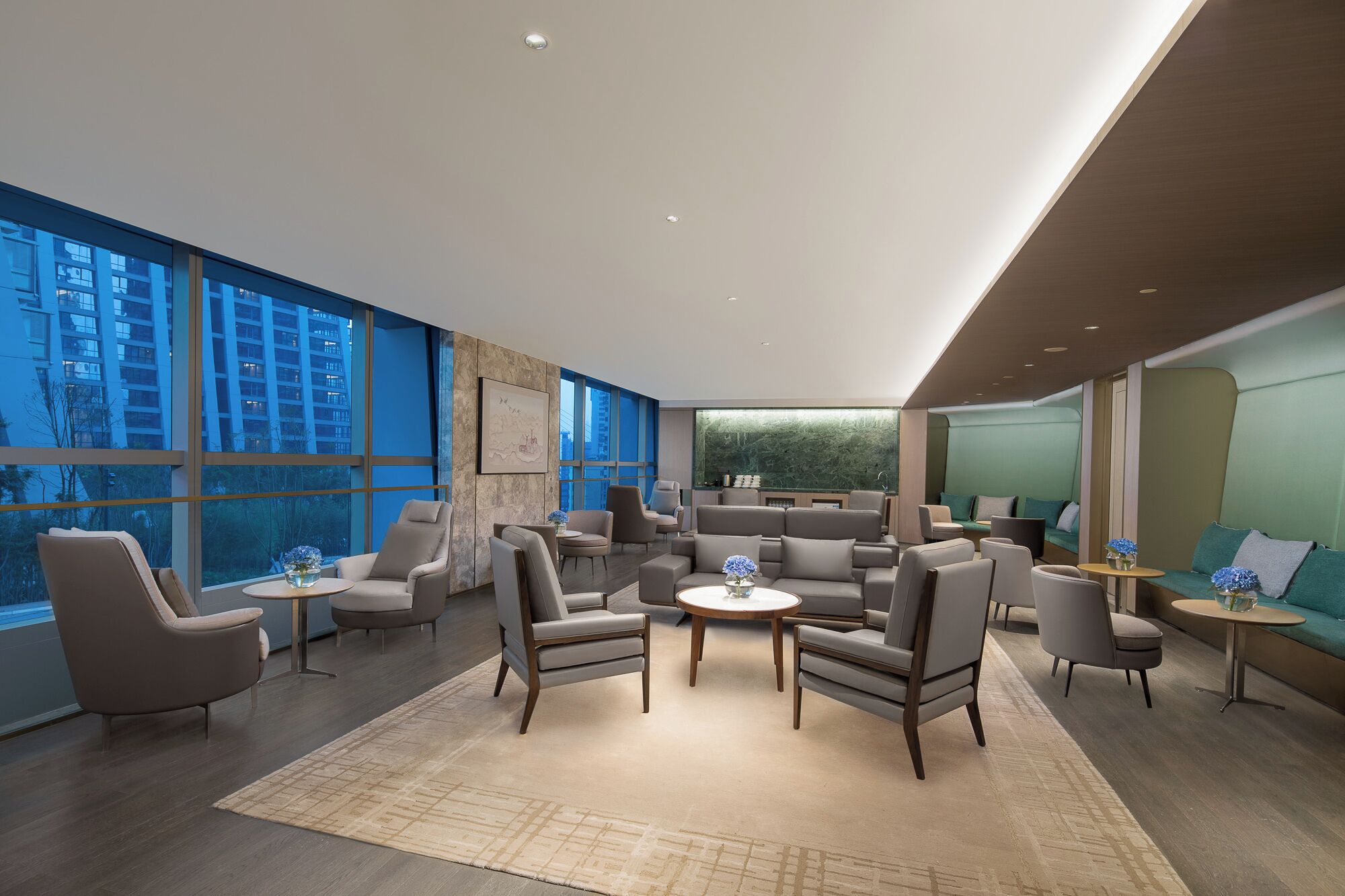 Una habitación de hotel moderna con ventanas amplias, una zona de estar central y vistas a un edificio.