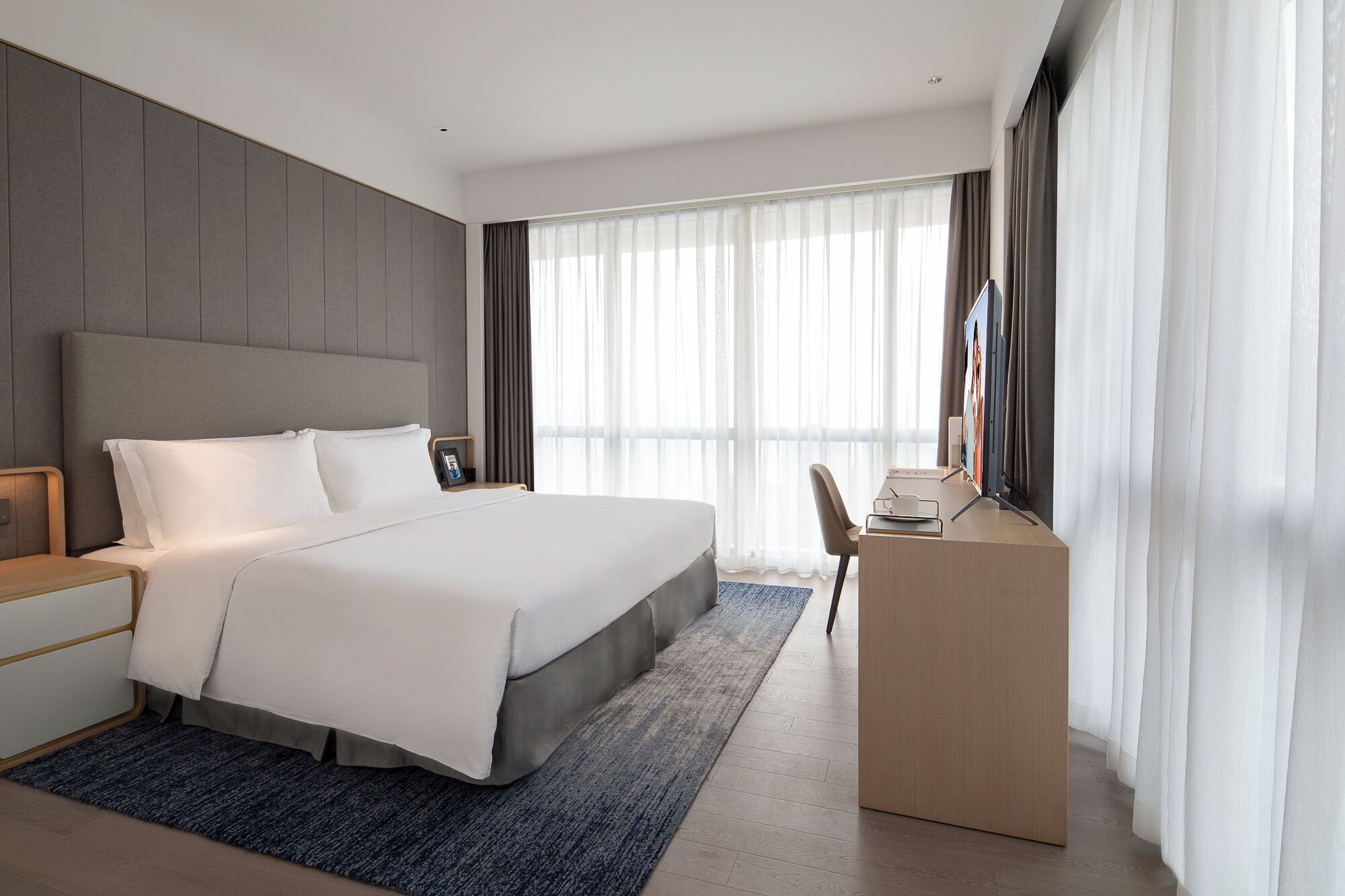 A modern hotel room with a large bed, a desk, and a television.