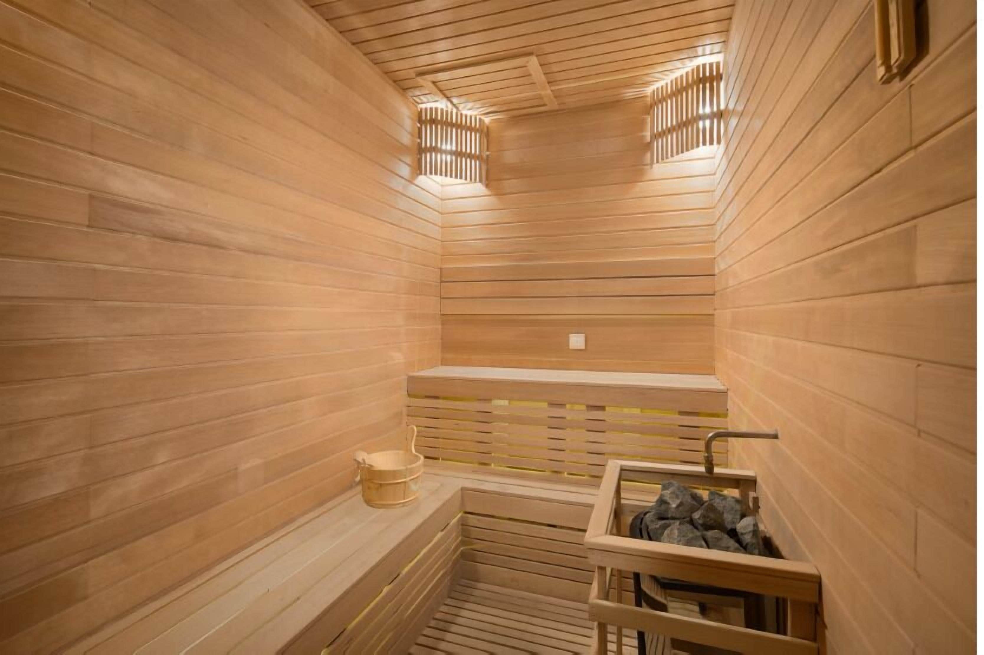 A sauna with wooden walls and benches, a small sink, and a bucket.