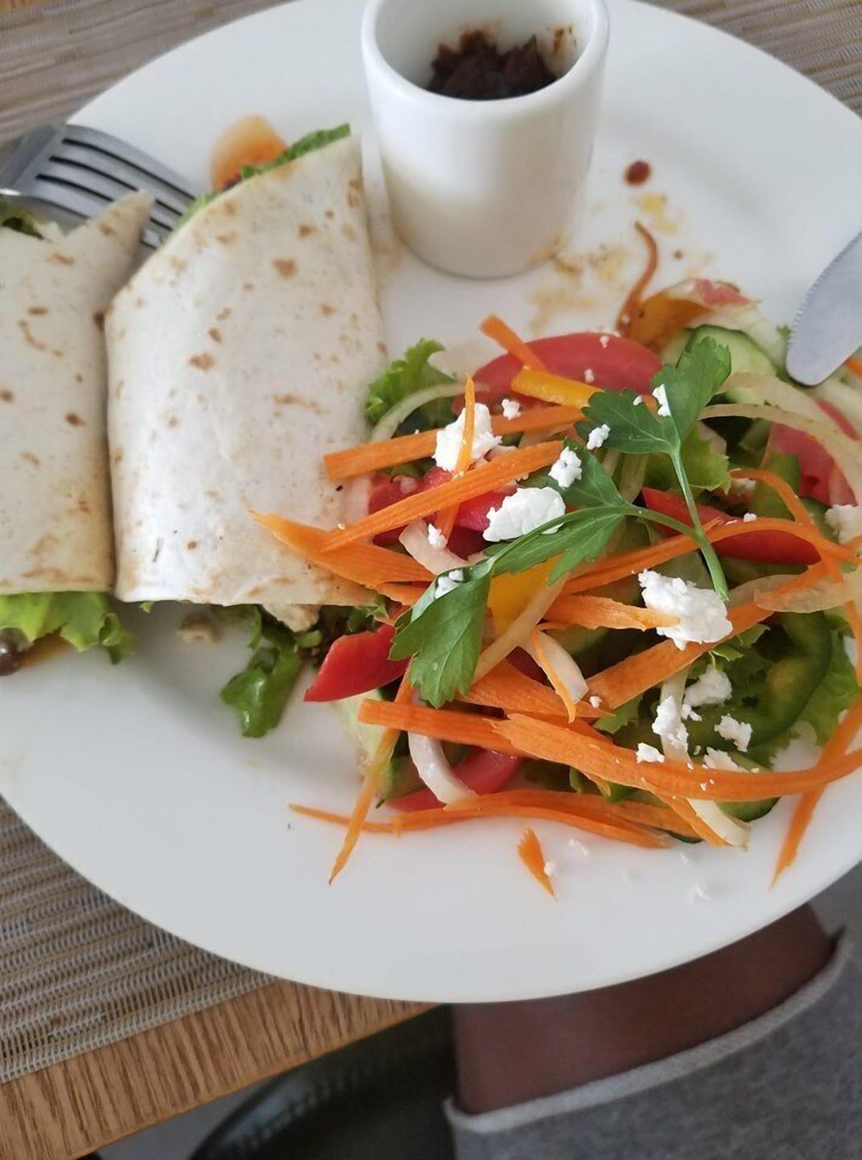 A plate with a salad, a small cup, and two wraps.