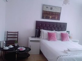 Un dormitorio con cama, mesita de noche, sillón y una pequeña mesa con una planta y una tetera.