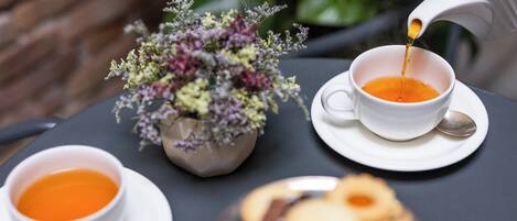 A table with two cups of tea, a teapot pouring tea, a small vase with flowers, and a plate of cookies.