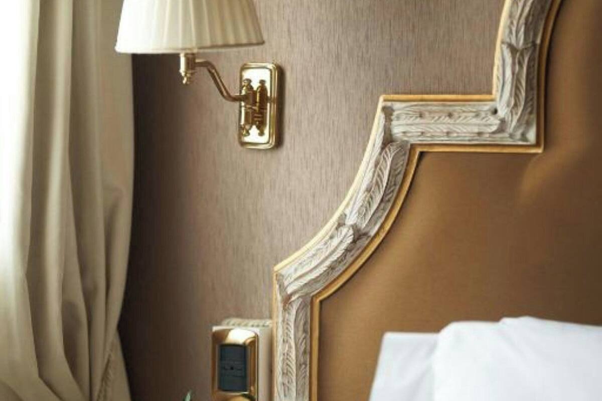 A hotel room with a bed, a bedside lamp, a small table with a vase of flowers, and a wall-mounted clock.