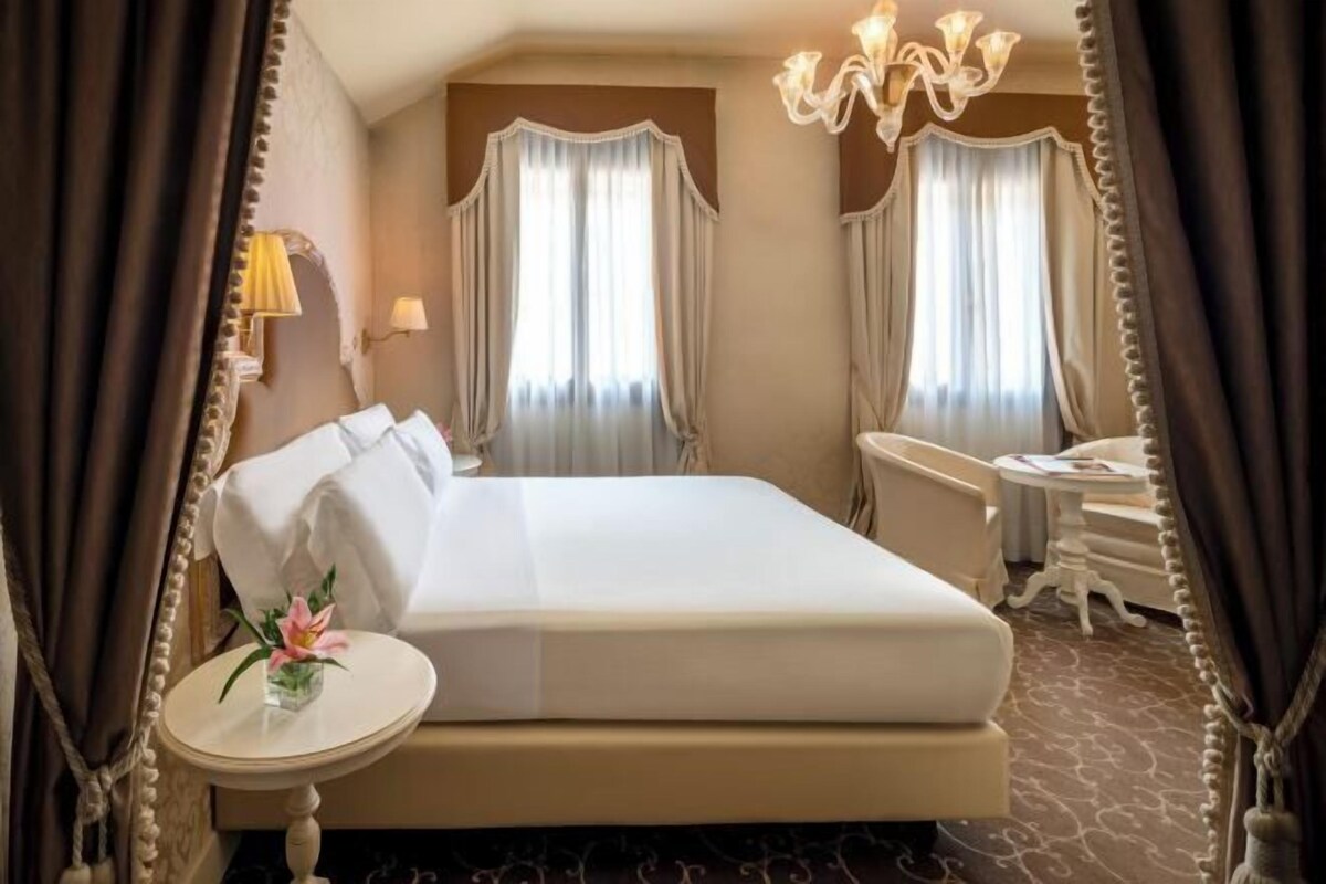 A hotel room with a large bed, a bedside table, a chair, and a desk.