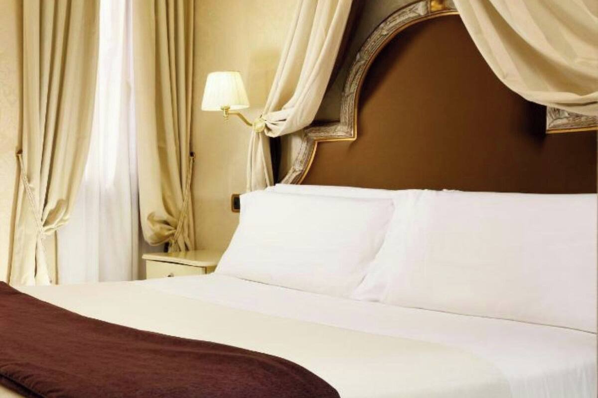 A neatly made bed with white linens, a brown throw blanket, and a headboard with a decorative frame.