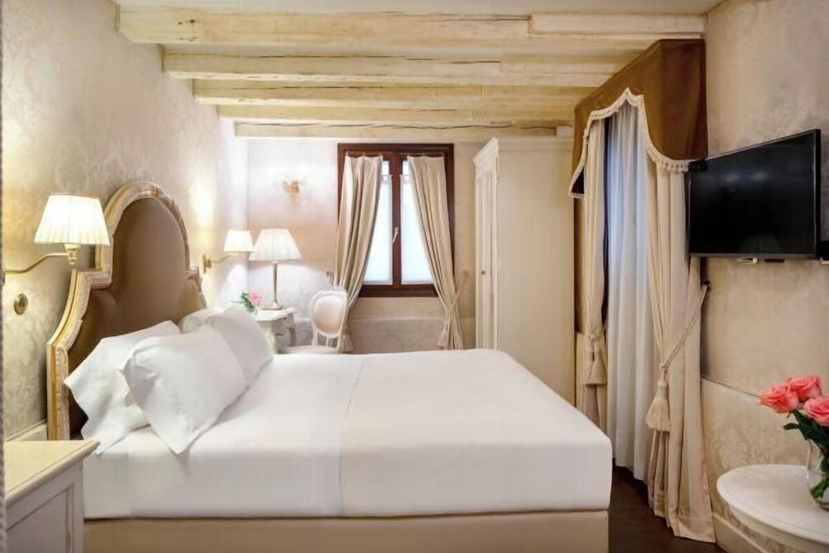 A hotel room with a bed, bedside lamps, a television, and a small table with a vase of flowers.