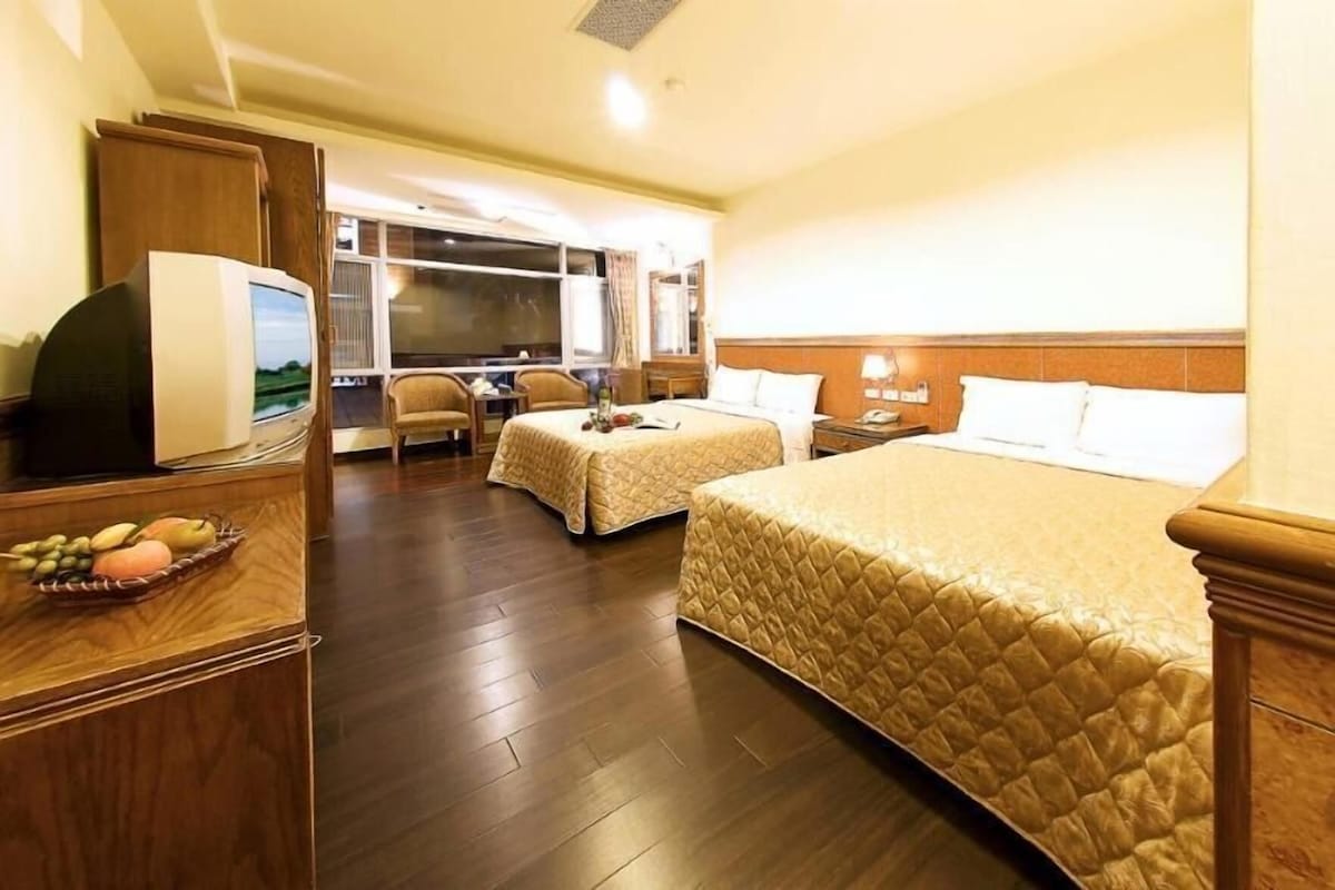 A hotel room with two beds, a desk, a chair, a television, and a fruit basket.