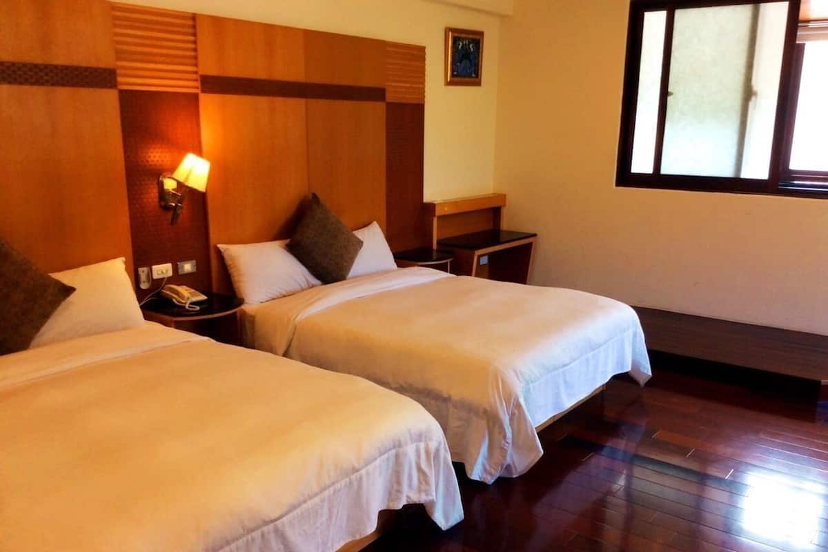 A hotel room with two beds, a nightstand, a lamp, and a window.