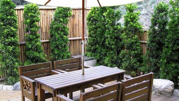A wooden deck with a table and chairs, surrounded by bamboo fencing and lush greenery.
