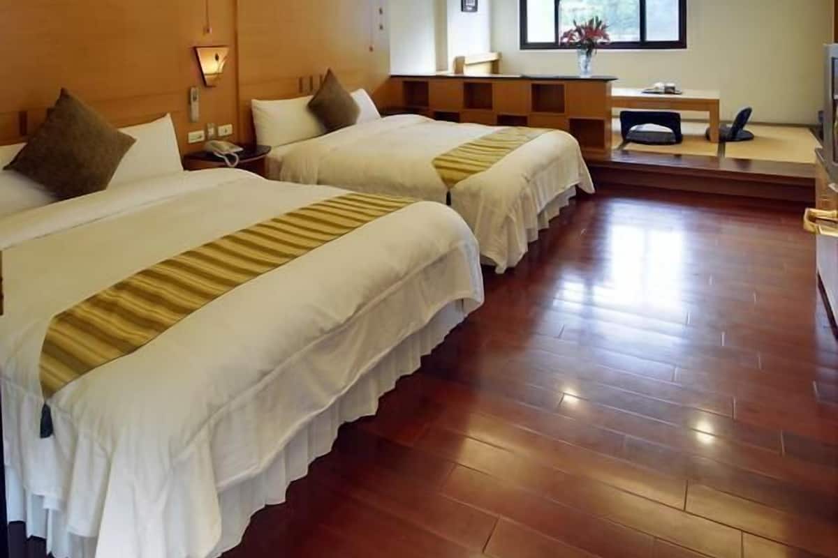 A hotel room with two beds, a desk, a chair, and a window with a view.