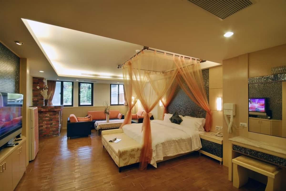 A bedroom with a four-poster bed, a television, a desk, and a seating area with a sofa and armchair.