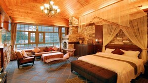 A spacious bedroom with a large bed, a stone fireplace, and a view of the outdoors through large windows. - Ming Lu Holiday Hotel (Ren'ai)