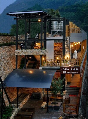 Un spa de varios niveles con paredes de piedra, muebles de madera y una zona de estar exterior cubierta.