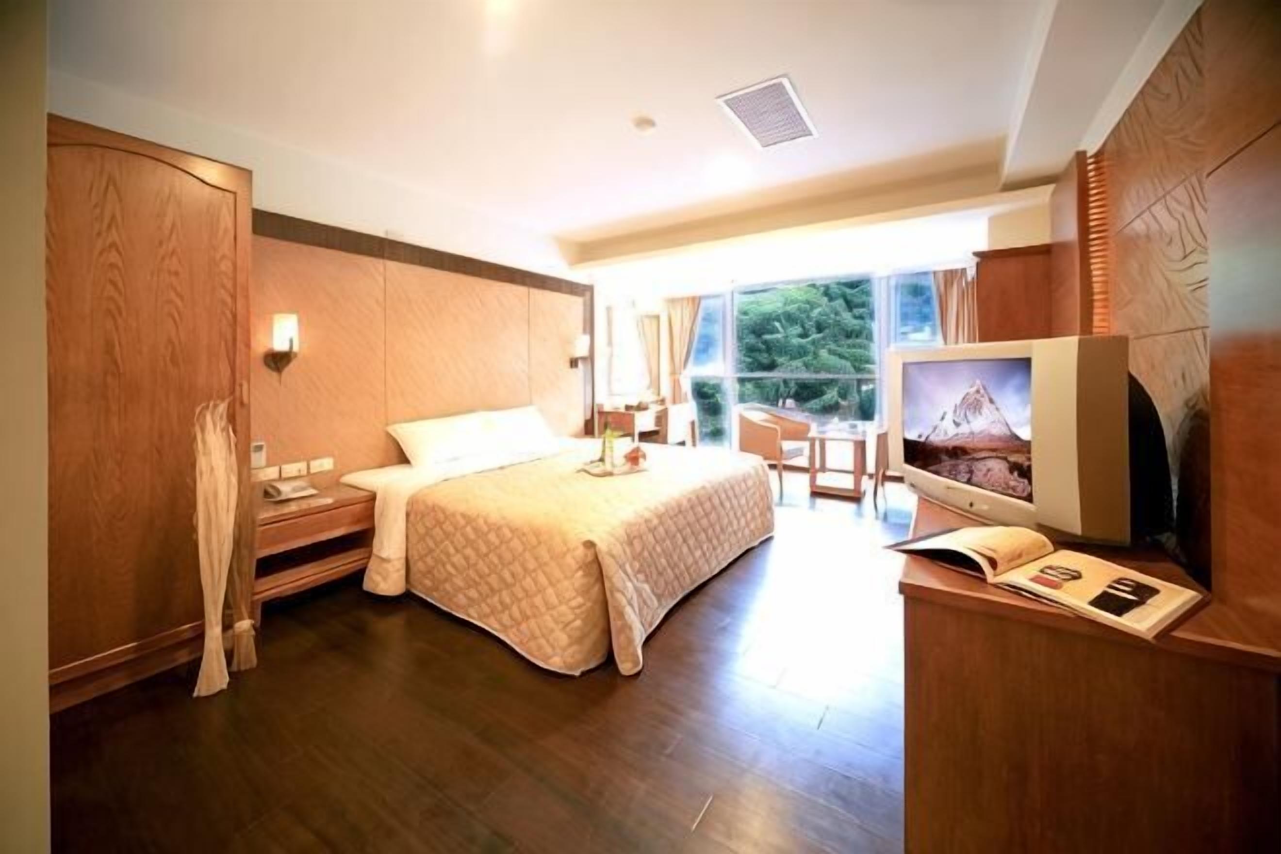 A hotel room with a large bed, a desk with a computer, a TV, and a view of the outdoors.