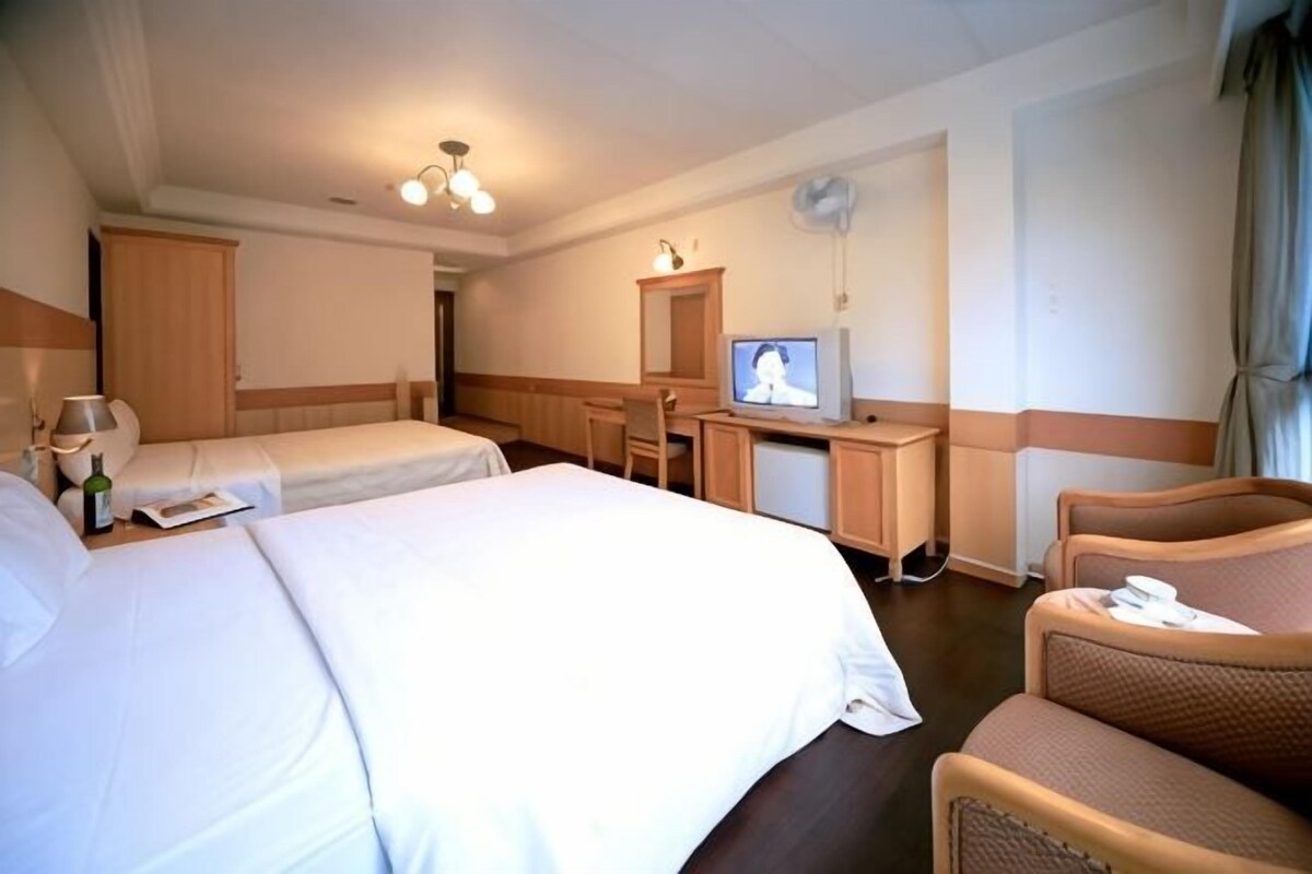 Habitación de hotel con dos camas, un escritorio con televisor, una silla y una mesita con una botella y vasos.