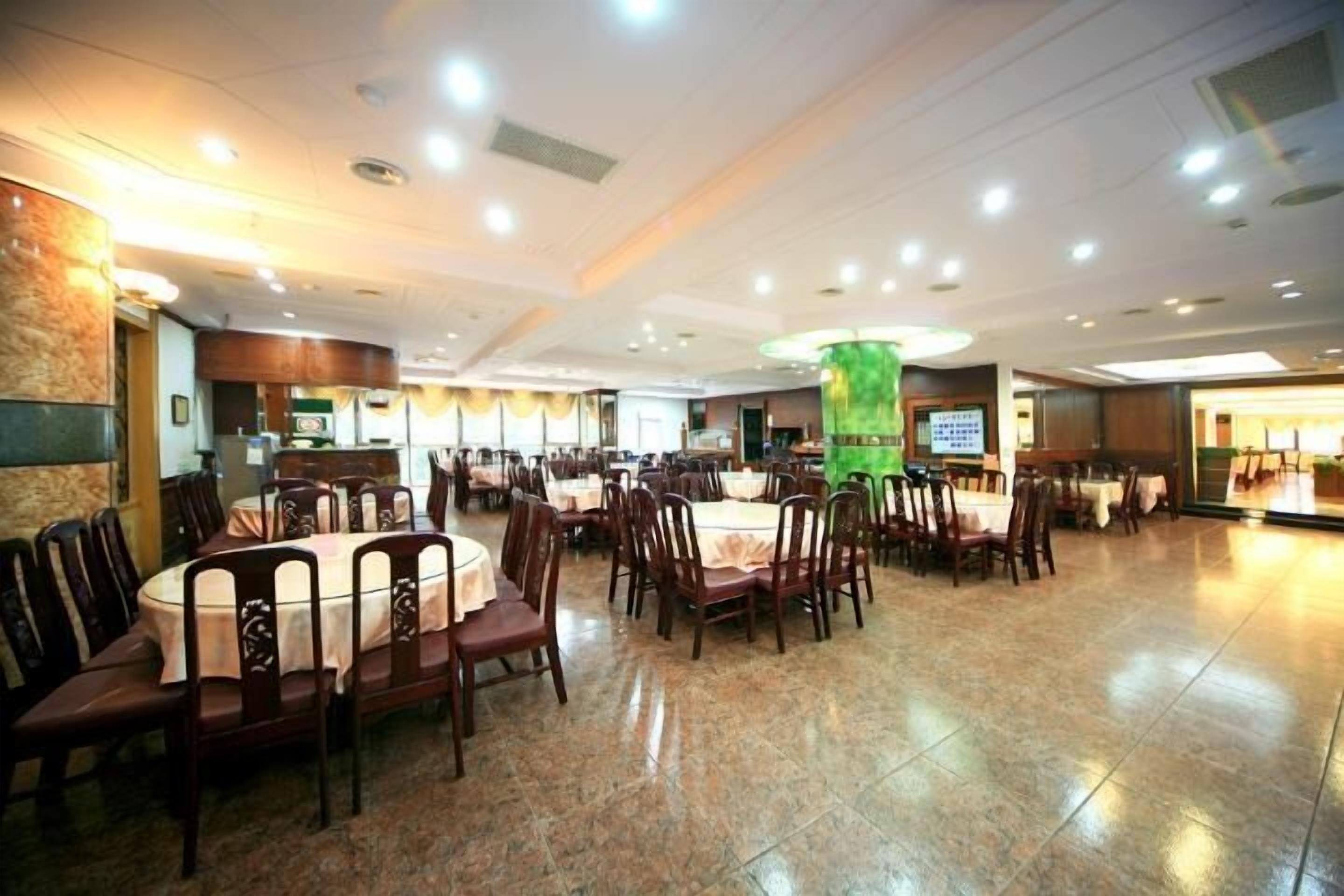 A spacious dining area with round tables and chairs, a central pillar, and a television screen.