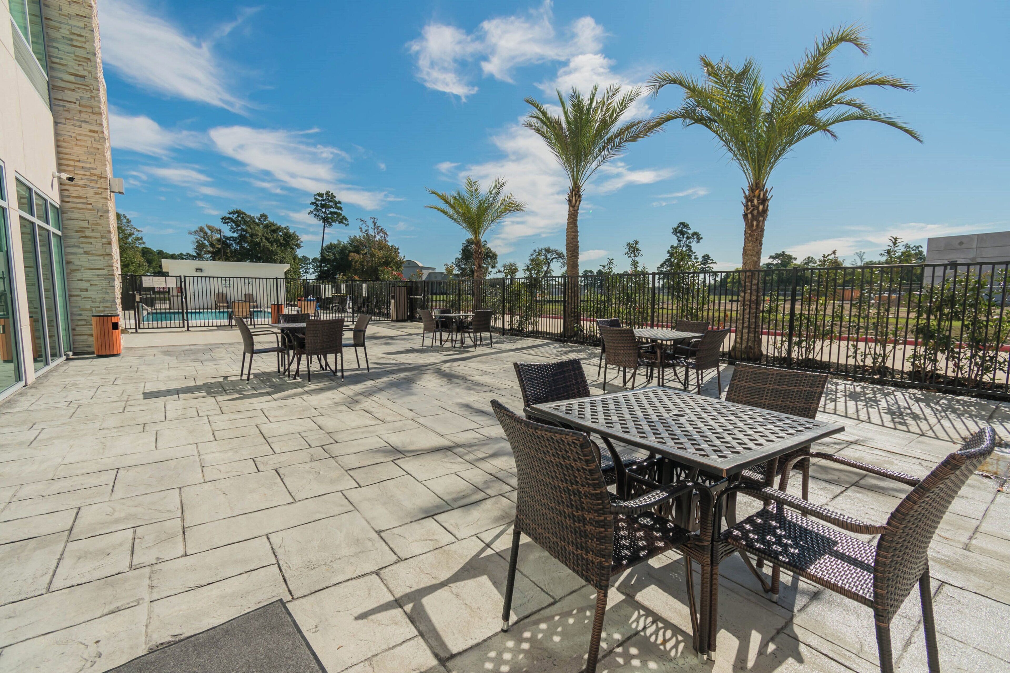 Un espace extérieur aménagé en terrasse, avec des tables et des chaises, une piscine et des palmiers.