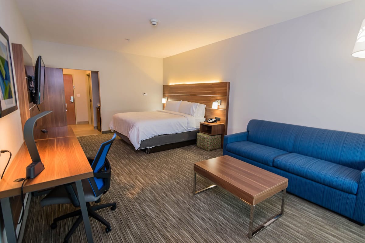A hotel room with a bed, a blue sofa, a wooden desk, and a computer.