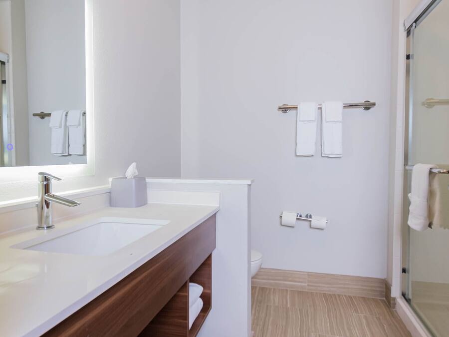 Une salle de bain moderne avec un grand miroir, deux lavabos, une douche et un espace douche fermé par des parois de verre.