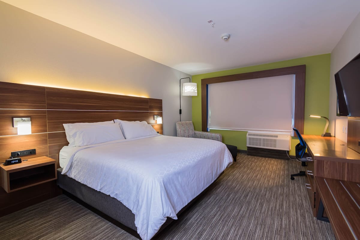 A hotel room with a large bed, a desk, a chair, and a TV.
