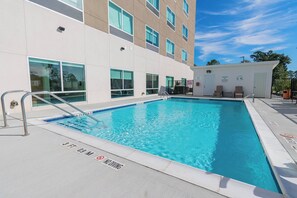 Una piscina rectangular con una escalera metálica, rodeada por un edificio de amplios ventanales y fachada blanca.