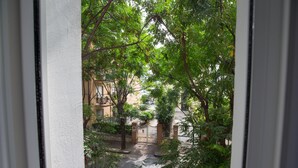 Vista attraverso una finestra su un cortile con un cancello, circondato da alberi ed edifici.