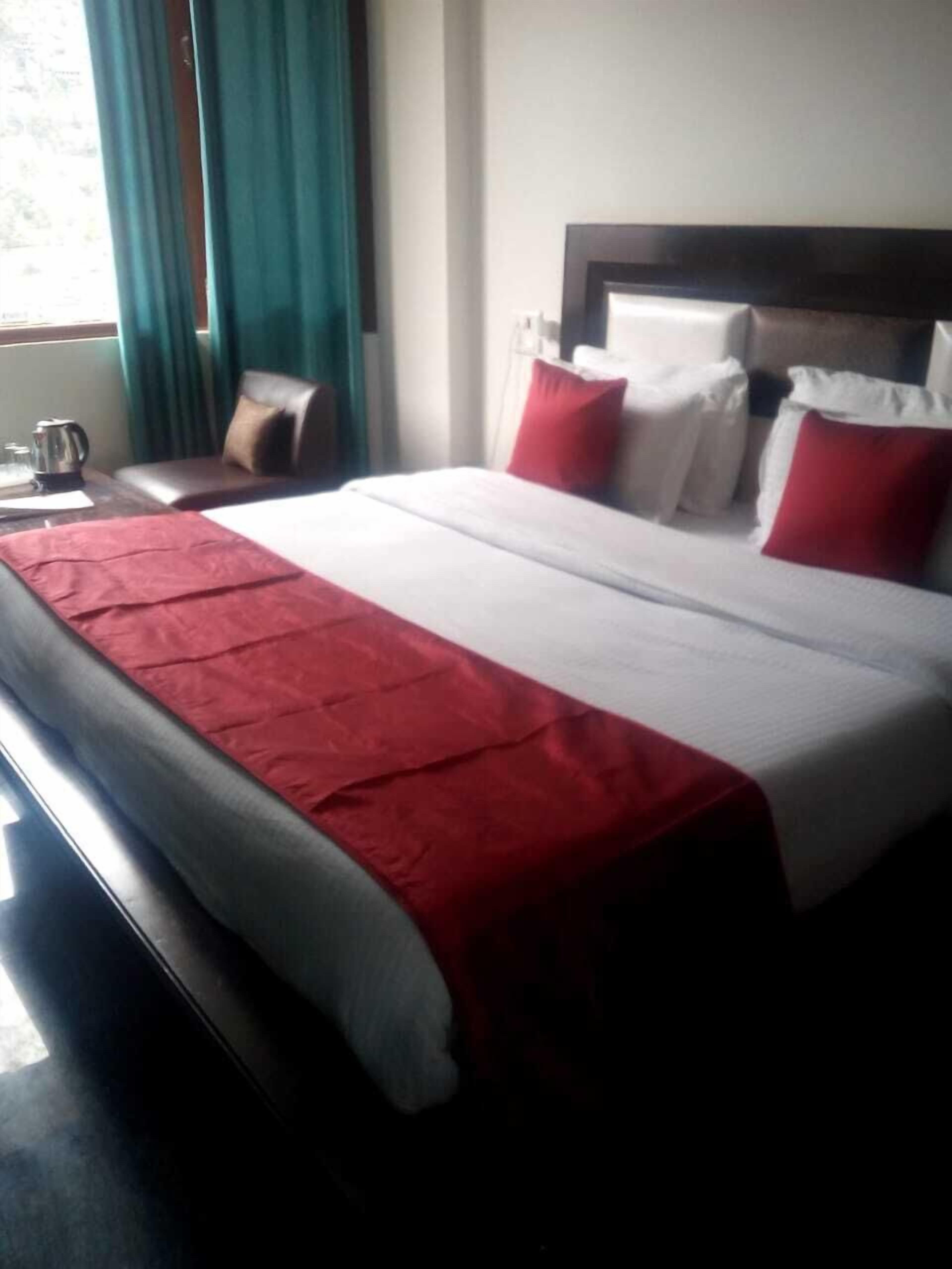 Habitación de hotel con una cama grande, una mesita de noche, una cafetera y una ventana con cortinas.
