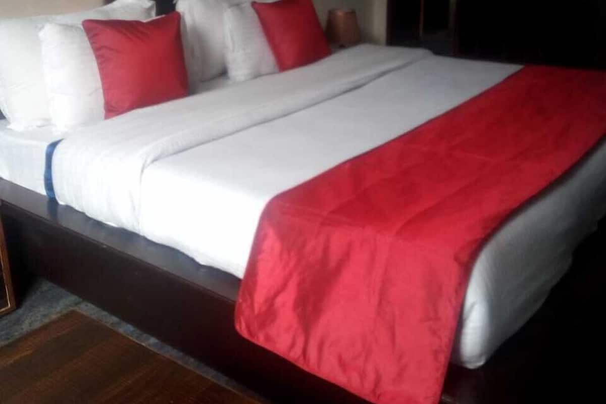 A hotel room with a large bed, a wooden headboard, and a red throw blanket.